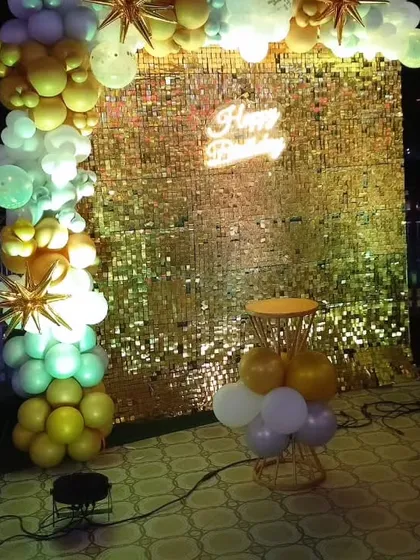The golden sequin wall photo booth with a cake stand, ready for the celebration.