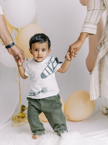 A baby boy takes his first tentative steps, holding his parents' hands. This is such a precious milestone to capture during a first birthday session.