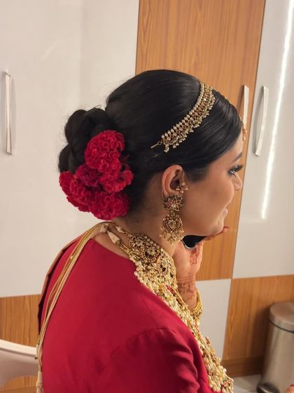 A sleek and grand bridal bun adorned with vibrant red flowers and a traditional matha patti, a classic look for a North Indian bride.