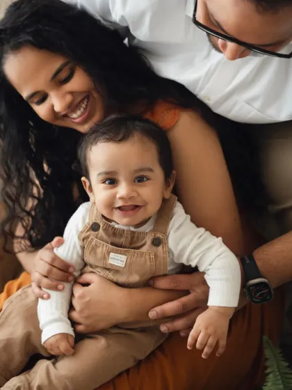 A sweet moment with parents looking down at their smiling baby. This is a lovely, intimate shot from a family photoshoot.