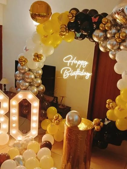 A 30th birthday party with a yellow, black, and white balloon arch and marquee numbers.
