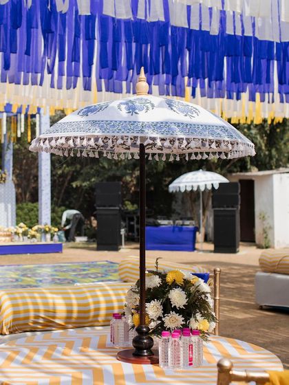 A beautiful printed umbrella provides shade and style for a guest table, featuring a yellow and white chevron tablecloth.
