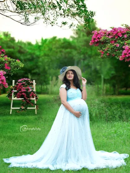 A peaceful moment in a beautiful garden setting. The mother-to-be, in a light blue gown and hat, looks serene among the flowers.