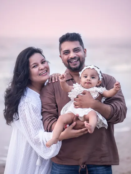 A happy family of three enjoying their time at the beach. The baby's playful wave and the parents' smiles make this a perfect candid family photo.