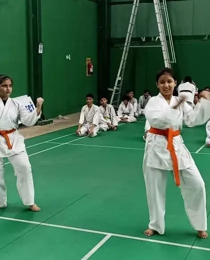 Two female students with orange belts performing their Kata for the examiners. Their confidence and synchronization are clearly visible.