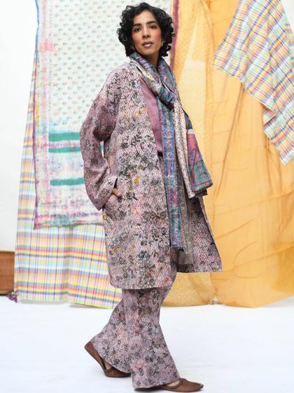 A full-length shot showcasing a layered, coordinated look from Wandering Silk. The model's confident stance and the backdrop of colorful textiles create a dynamic and stylish fashion portrait.