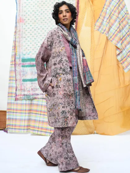 A full-length shot showcasing a layered, coordinated look from Wandering Silk. The model's confident stance and the backdrop of colorful textiles create a dynamic and stylish fashion portrait.