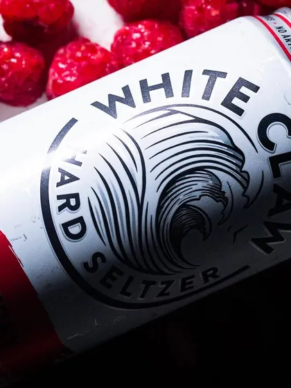 A can of Raspberry White Claw styled with fresh raspberries. This visually reinforces the flavor and makes the product look fresh and natural.