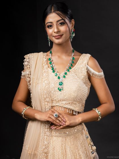 A model wearing a beautiful cream lehenga and a stunning emerald and diamond necklace set. This image is a perfect example of a high-end ethnic jewellery shoot.