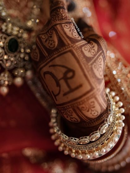 A close-up of the bride's personalized monogram, 'PR', showcasing the deep and even stain achieved with natural henna.