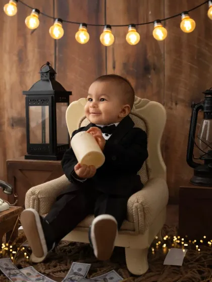 A sweet, smiling baby boy in his tuxedo, holding a candle. The warm lighting creates a cozy and classic feel for this portrait.