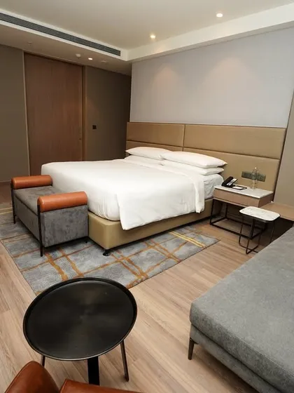 A full view of a modern hotel bedroom suite, including the king-sized bed, chaise lounge, and minimalist decor, conveying a sense of calm and comfort.