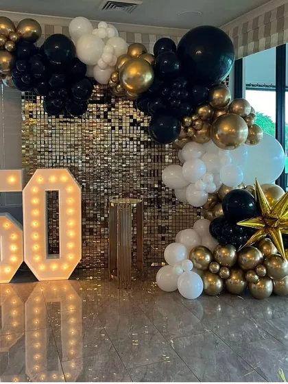 A bold and beautiful 50th birthday setup. The gold sequin wall is paired with a dramatic black, gold, and white balloon arrangement.