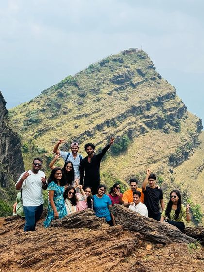 A fun group photo on a rocky outcrop with a stunning mountain peak in the background.