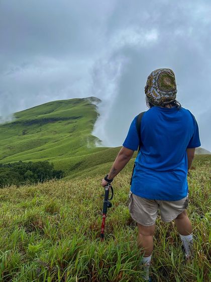 A trekker looking out at the sharp, misty ridge of Netravathi Peak. The trail offers some of the most dramatic views in Karnataka.