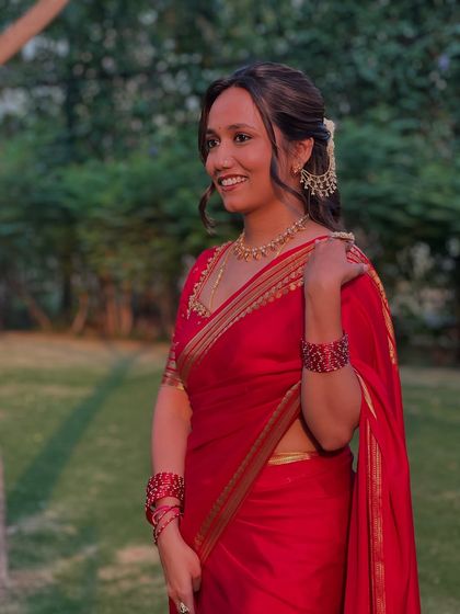 A happy portrait of the client, her traditional half-updo and red saree creating a timeless look.