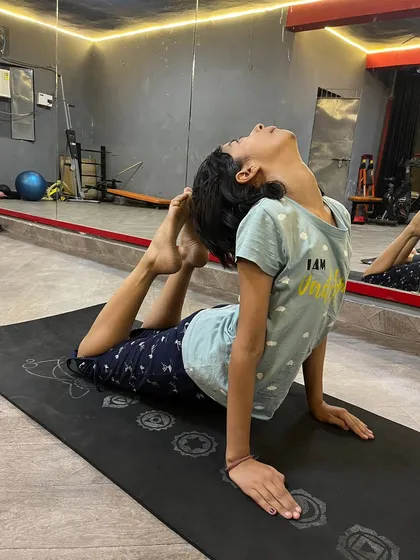 A young student working on her back flexibility in a variation of king pigeon pose.