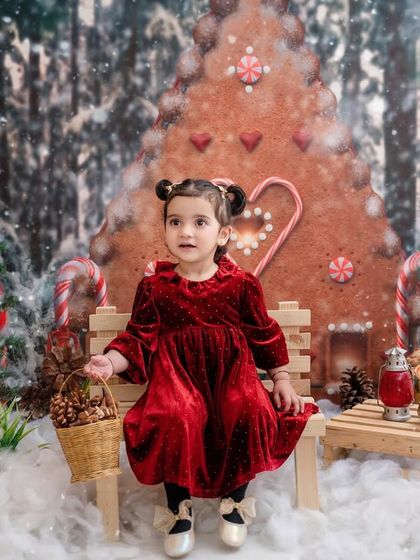 Celebrating her second winter, this little girl sits in a snowy scene, complete with a gingerbread house and candy canes.