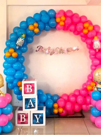 A classic 'boy or girl' themed baby shower balloon ring. The decoration uses pink and blue balloons, 'BABY' blocks, and baby-shaped foil balloons.