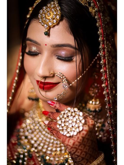A close-up of a bride, highlighting her glittery eye makeup, red lipstick, and traditional jewelry.