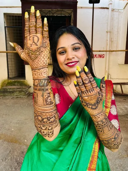 The joy on a bride's face says it all. Here is a happy client showing off her full bridal mehndi, complete with personalized initials, looking radiant on her special day.