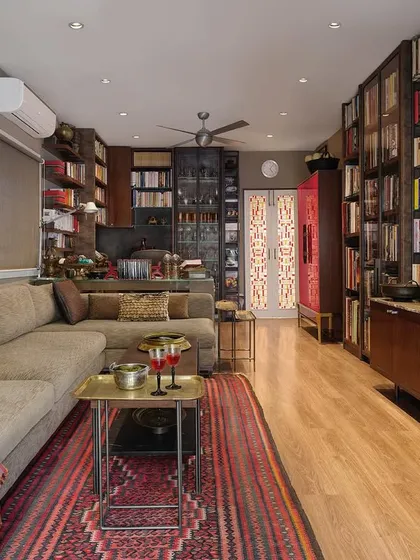 The book-lined linear study in the Courtyard Home, a cozy refuge for reading and relaxing. The space is filled with personal collections, including a minimalist painting by Shobha Broota and a custom-designed 'Raspberry Bar'.
