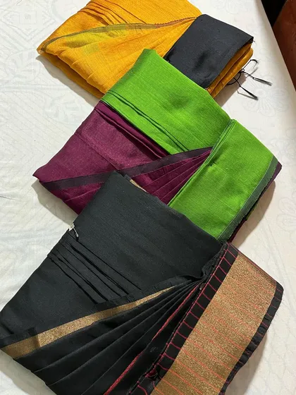 A collection of customer sarees in black, green, and yellow, all neatly folded.