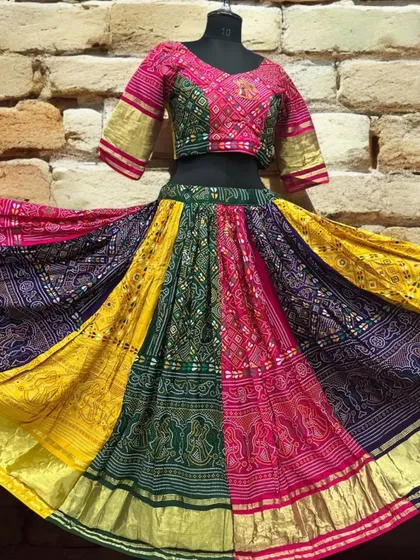 A unique multi-panel lehenga skirt in shades of pink, green, yellow, and blue, showcasing traditional bandhani prints. The embroidered blouse completes this colorful dandiya-ready look.