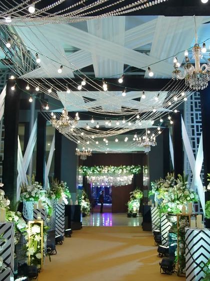 Modern and graphic, this entrance uses bold black structural elements and white draping, lit by strings of Edison bulbs. The design is perfect for a contemporary wedding or a chic corporate event.