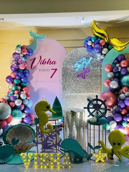 An enchanting 'Under the Sea' mermaid theme, using a palette of purple, teal, and pink chrome balloons, complete with a neon mermaid sign and aquatic props.