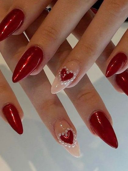 Classic red with a romantic twist. These sharp stiletto nails feature a deep chrome red, with an accent nail showcasing a heart made of tiny pearls on a nude base.