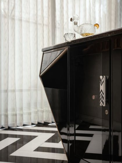 A detail of the custom bar cabinet, showing the angular design and chevron-patterned handles. The high-gloss finish reflects the light, adding to the room's sophisticated and dramatic feel.