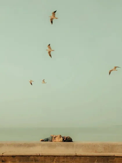 A person lies on the sea wall at Marine Drive, with seagulls flying overhead. This minimalist composition captures a moment of complete relaxation and surrender to the city's seaside atmosphere.