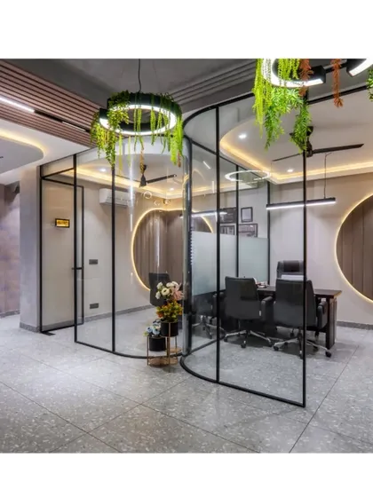 A wider view of the office, showing the curved glass meeting rooms and the open, collaborative corridor. The hanging circular lights with greenery add a biophilic touch to the modern design.