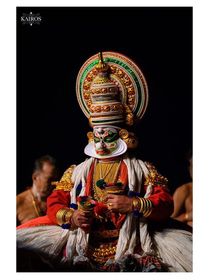 A portrait of a Kathakali artist in full costume. The rich colors and intricate details of the traditional attire are highlighted against a dark background.