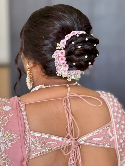 A classic bridal bun adorned with a beautiful floral gajra and pearl details. This hairstyle is timeless and complements the pastel pink lehenga perfectly.