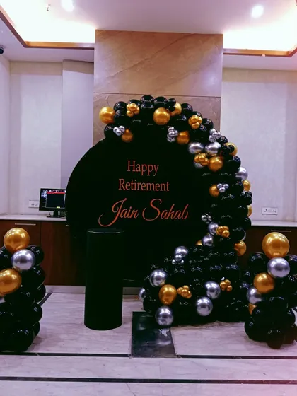 A sophisticated and stylish retirement party decoration. This setup features a classy black, gold, and silver balloon arrangement around a personalized "Happy Retirement" backdrop, perfect for honoring a distinguished career.