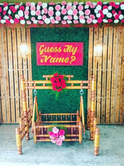 Make the name reveal a special moment with our custom signs. This setup features a traditional wooden cradle (jhula) against a rustic wooden panel backdrop with a "Guess My Name?" sign to engage your guests.