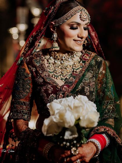 A beautiful portrait of a bride holding a bouquet of white roses, her rich green and maroon lehenga creating a striking color contrast.