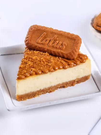 A perfect slice of my eggless baked Biscoff Cheesecake. You can see the thick biscuit base, the creamy cheesecake layer, and the generous topping of Biscoff spread and a whole biscuit.