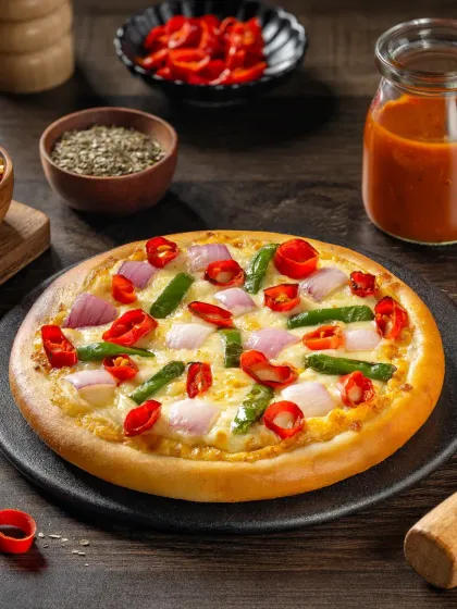 A spicy vegetable pizza with red chilies, onions, and capsicum, styled with fresh ingredients to highlight its heat.