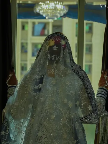 An artistic and moody shot of the bride behind a curtain. The silhouette and the way the light filters through her veil create a mysterious and beautiful image.