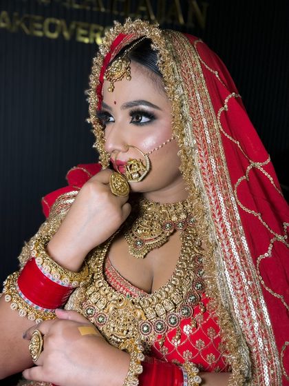 A side profile of a bride in a stunning red and gold lehenga. The focus is on her intricate jewelry and the flawless finish of her HD makeup.