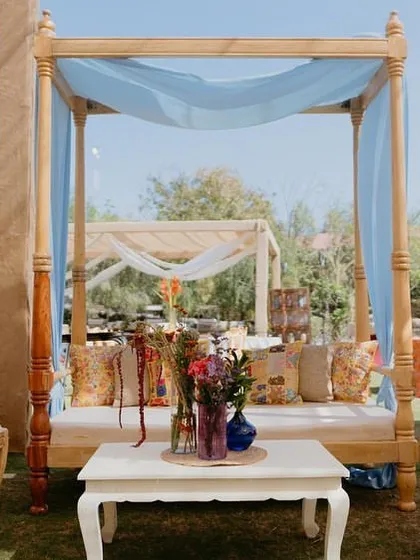A four-poster daybed with light blue drapes provides a comfortable and stylish seating option at the 'Rajasthani Folklore' Mehendi.