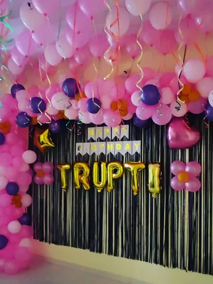 A birthday backdrop created with a black shimmer curtain and a pink and purple balloon garland. The ceiling is covered with pink balloons, creating a fully decorated party corner.