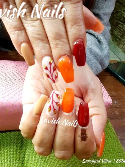 An autumnal color palette with orange, red, and nude nails, featuring a delicate hand-painted branch design.
