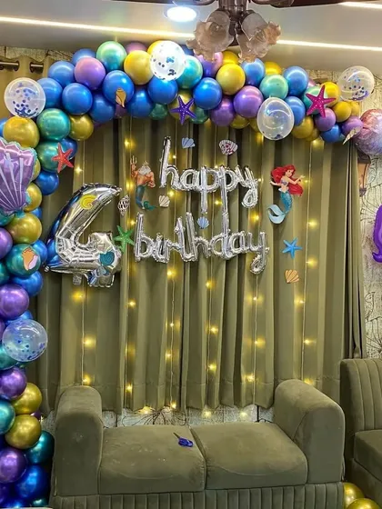 A clear shot of the mermaid party setup, showing the 'Happy Birthday' foil letters and character cutouts.