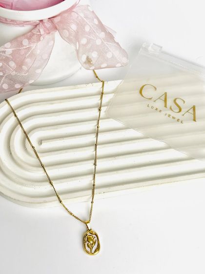 A gold pendant necklace with a floral design, shot in a simple, elegant flatlay. This highlights the product's details while maintaining a soft, feminine aesthetic.