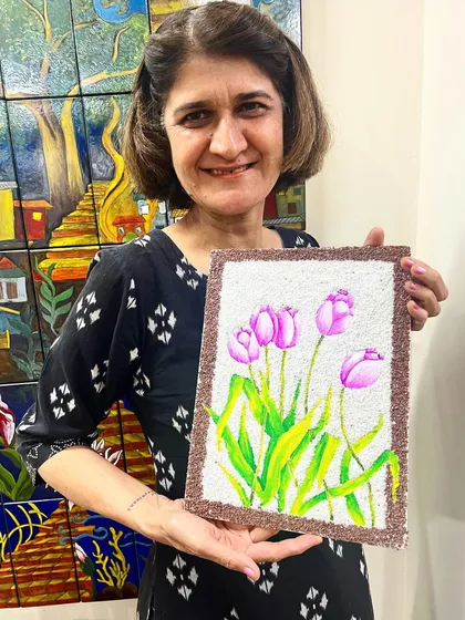 A proud student holding her finished mixed-media artwork of tulips, which combines painting with a textured rice background.