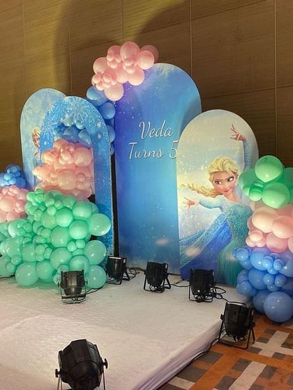 A magical Frozen-themed stage for a 6th birthday, with backdrops of Elsa and Anna, and balloon arrangements in icy blue, green, and pink.